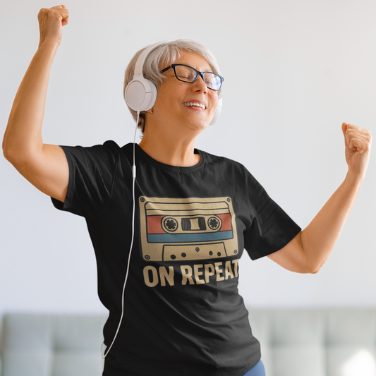 Person wearing a black t-shirt with a cassette tape design and 'On Repeat' text, listening to music with headphones.