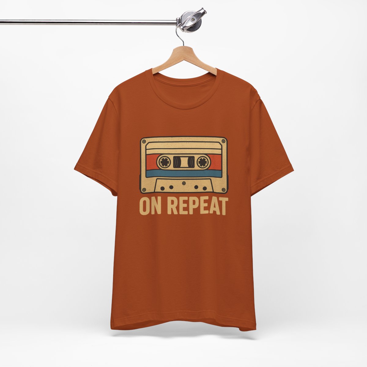 Orange t-shirt with cassette tape graphic and 'On Repeat' text on a hanger against a white background