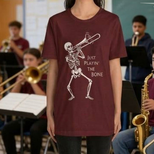 Person wearing a maroon t-shirt with a skeleton playing an instrument design, standing in front of a band practice.