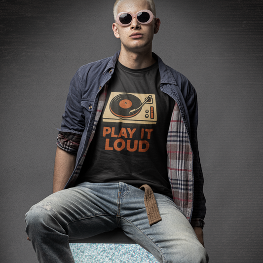 Person wearing a 'Play It Loud' with vintage turntable t-shirt sitting on a vintage television set with a dark background.