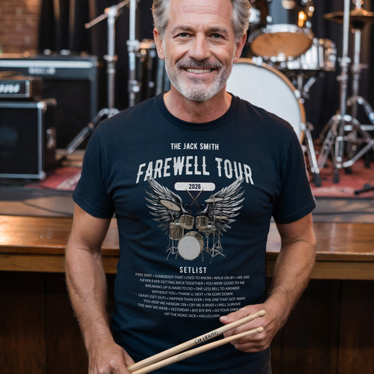 Man wearing a 'The Jack Smith Farewell Tour' retirement t-shirt holding drumsticks in a music studio setting.