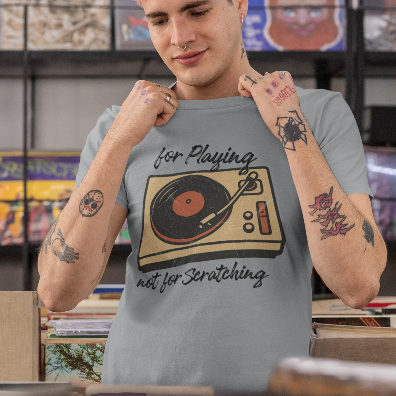 Person wearing a gray t-shirt with a vintage turntable and the words "for Playing, not for Scratching" graphic design in a record store